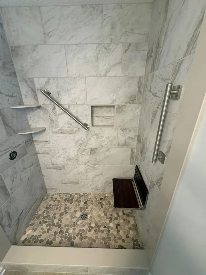 Marble-tiled shower with two grab bars and a fold-down teak seat